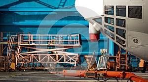 The nose of the aircraft against the blue hangar. mobile ladders, lower observation windows