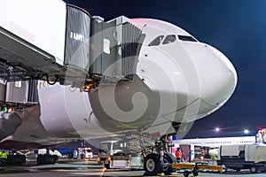 Nose and cockpit airplane at passenger gangway of the terminal building at the airport at night, aircraft flight maintenance.