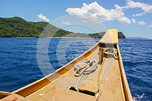 The nose of a wooden boat with ropes on a background of blue sea