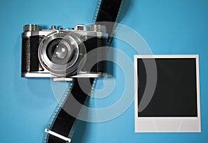 Nostalgic concept blank instant photo frame on blue background with old retro vintage camera with film strip