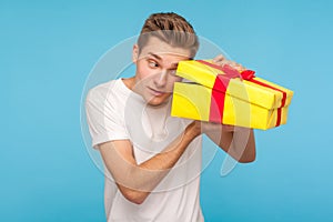 Nosy impatient man in white t-shirt looking inside gift box with curious happy expression