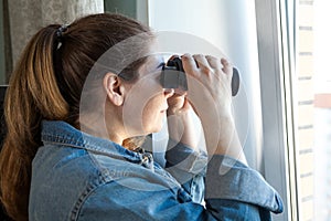 Nosy woman peering through window with binoculars, a domestic room