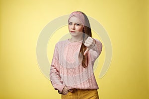 Not cool. Frustrated displeased and disagree cute young woman wearing knitted sweater frowning showing thumb-down