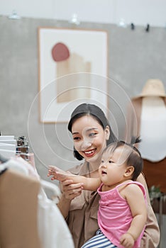 It is not easy to be a working mom! Young beautiful designer  working on her atelier while standing with her baby girl