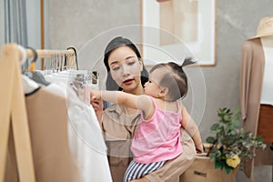 It is not easy to be a working mom! Young beautiful designer  working on her atelier while standing with her baby girl