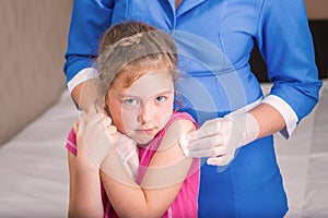 Not happy and scared face of a little girl is after vaccination. The child is afraid to be vaccinated. A gloved nurse applies