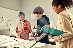 Not just design but create. Young male designer cutting white fabric textile for T-shirts in a studio. Group of creative