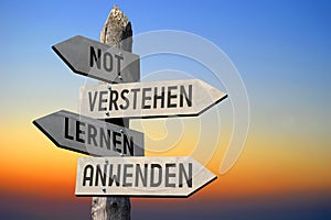 Not, verstehen, lernen, anwenden - German/ need, undestand, learn, apply - English - wooden signpost, sunset sky