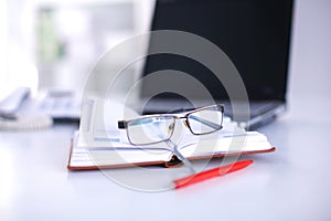 A note book, laptop, pen, graph paper document on the office desk table behind white blind