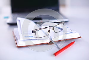 A note book, laptop, pen, graph paper document on the office desk table behind white blind