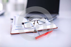 A note book, laptop, pen, graph paper document on the office desk table behind white blind