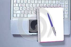 A note book, laptop, pen, graph paper document on the office desk table behind white blind