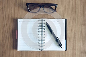Top view on a note book with pen and glasses on a workdesk