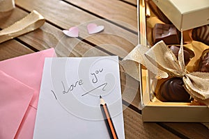 Note with love message and chocolates on wooden table