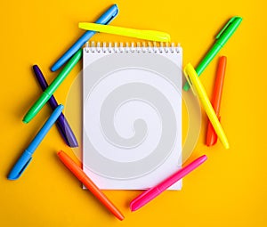 Note pad with empty space for text, colorful felt tip pens around on yellow background