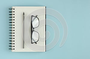 Note pad with eyeglasses and pencil composition on blue background
