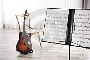 Note stand with music sheets and blurred acoustic guitar on background.