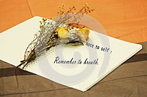 Note to self - Remember to breath. With dried white roses flowers arrangement with a note on a white book.