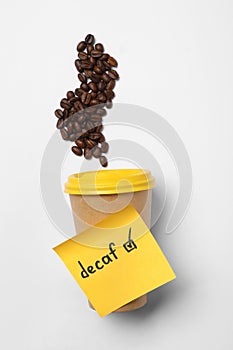 Note with word Decaf attached to takeaway cup and coffee beans on white background, flat lay