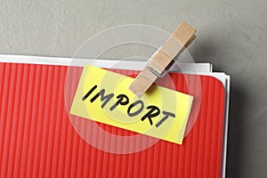 Note with word Import attached to folder of documents on grey table, top view