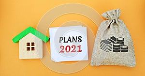 A note with the words plans 2021, a house and a money bag. Real estate concept. Family budget planning. Investments, plans,
