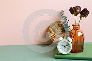 Notebook, alarm clock, vase of dry flower on green desk. pink wall background