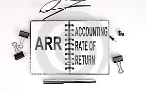 Notebook with ARR ACCOUNTING RATE OF RETURN on table with office tools