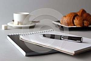 Notebook, ballpoint pen, coffee Cup and croissants