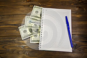 Notebook with ballpoint pen and dollar banknotes on the wooden desk
