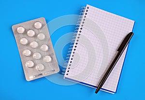 Notebook, black pen and pills on a blue background. Health