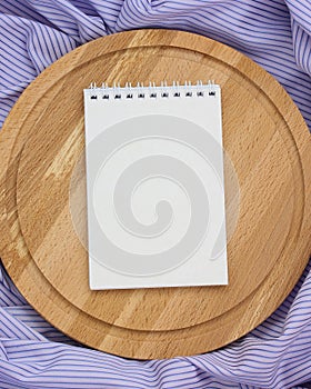 Notebook with blank cover and circular cutting Board on a purple striped tablecloth