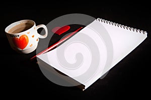 Notebook blank, cup of coffee, red heart on the black background. Top view with copy space. Love and Valentine`s Day concept