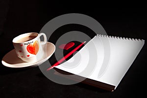 Notebook blank, cup of coffee, red heart on the black background. Top view with copy space. Love and Valentine`s Day concept