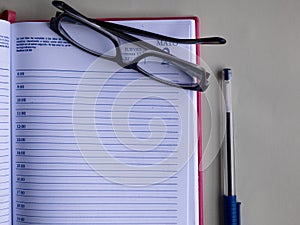 A notebook, blue pen and eyeglasses.
