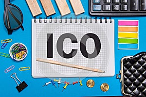 A Notebook with Business notes initial coin offering ICO with office tools on blue background.