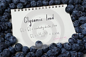 Notebook with calculated glycemic load for blueberries surrounded by fresh berries, closeup