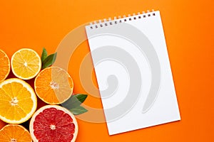 Notebook and citruses fruits on orange background, fruit flatlay, summer minimal compositon with grapefruit, lemon