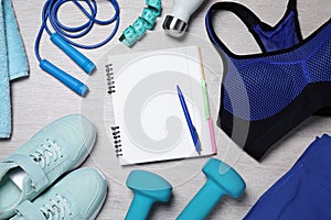 Notebook, clothes and sports equipment on white wooden table, flat lay. Personal training