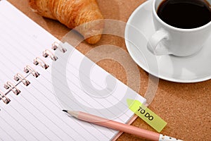 Notebook, coffee and croissant on a cork background