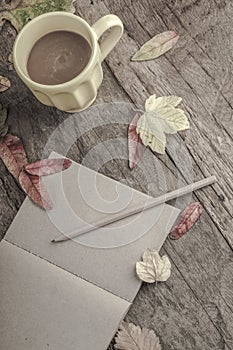 Notebook and coffee on wooden table decorated with dried leaves
