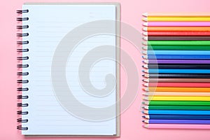 Notebook and colored pencils on pink background