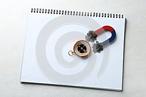 Notebook, compass and magnet with iron powder on light background, top view.