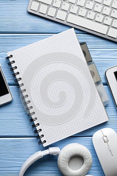 Notebook with copy space, headphones and computer mouse and keyboard on blue table