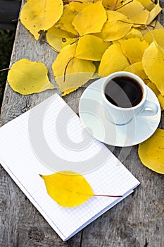 Notebook, cup of coffee and yellow autumn leaves