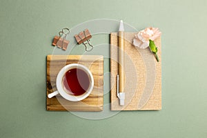 Notebook, cup of tea, clip, pen, carnation flower on green background