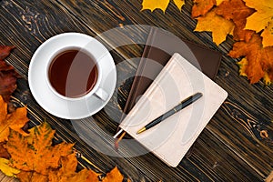 Notebook diary Cup of tea on a pile of bright autumn leaves against a dark wooden table