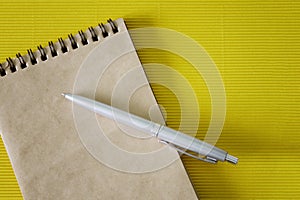 Notebook or diary made of eco-friendly recycled paper and a silver fountain pen lie on a yellow textured anti-stress surface. Copy