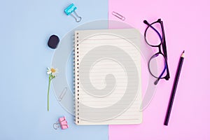 Notebook ,Eyeglasses,Black pencil,Eraser,Paper Clips and White Flower on Pink and Blue Background