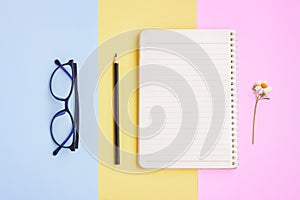 Notebook ,Eyeglasses,Black pencil and White Flower on Pink,Yellow and Blue Background