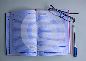 A notebook, eyeglasses and a blue pen.
